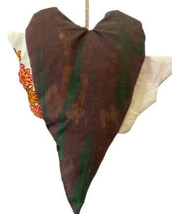 Herzförmiges Stoffobjekt in grün-brauner Batikoptik mit asymmetrischen Flügeln – einer aus weißer Baumwolle, der andere mit farbigem Waxprint-Muster in Rot, Gelb und Orange.