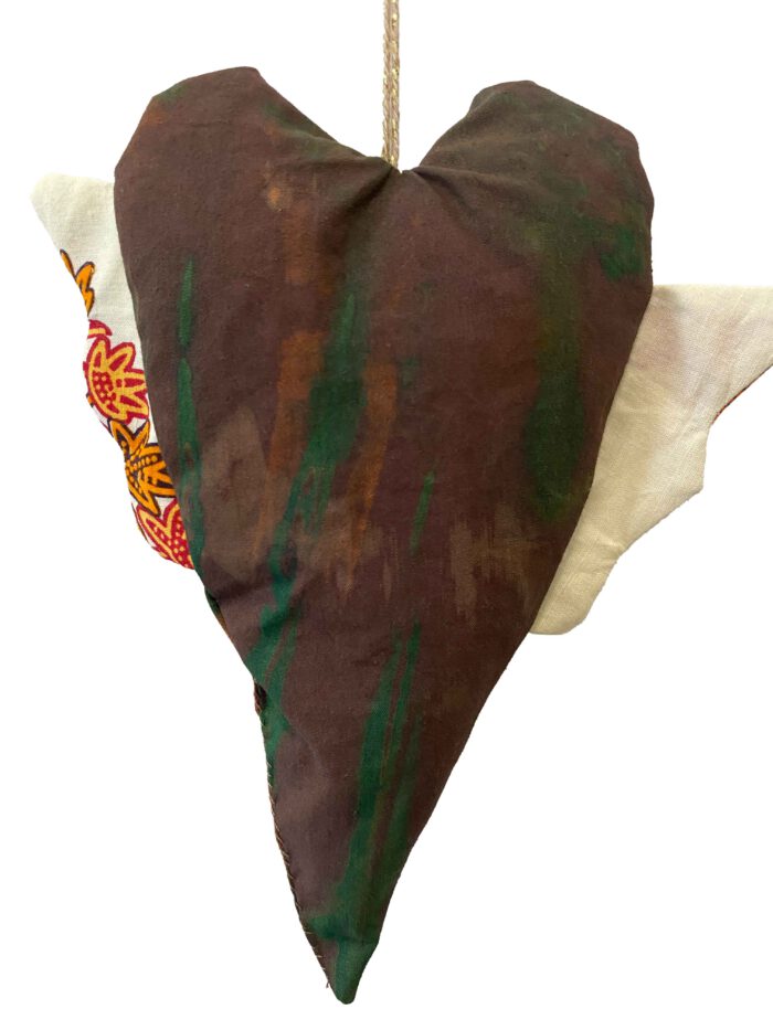 Herzförmiges Stoffobjekt in grün-brauner Batikoptik mit asymmetrischen Flügeln – einer aus weißer Baumwolle, der andere mit farbigem Waxprint-Muster in Rot, Gelb und Orange.