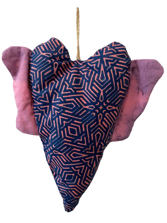 Handgemachtes Herz mit grafischem Muster in Blau und Pink sowie Flügeln aus rosa-batikfarbenem Stoff, aufgehängt an einer naturfarbenen Kordel mit Goldakzent.