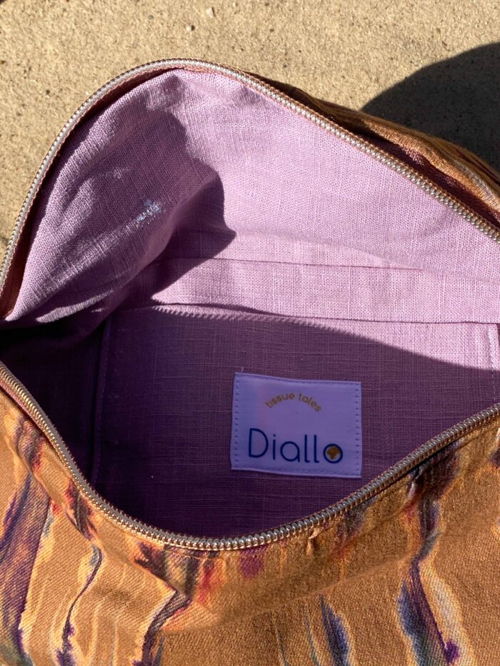 Bauchtasche aus afrikanischem Batikstoff in warmen Ocker- und Violetttönen, innen mit lilafarbener Fütterung und Label „Diallo tissue tales“.