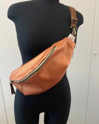 Kupferfarbene Kunstleder-Bauchtasche (Belly Bag) mit goldfarbenem Reißverschluss und braunem verstellbarem Schulterriemen, inspiriert von afrikanischer Mode, präsentiert auf einer schwarzen Schneiderpuppe.