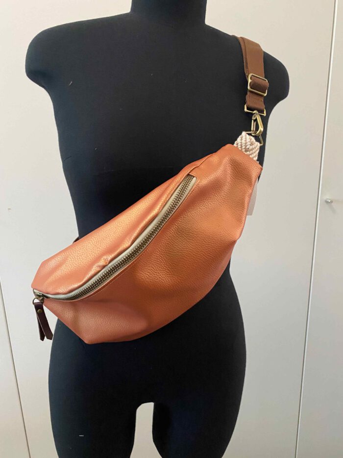 Kupferfarbene Kunstleder-Bauchtasche (Belly Bag) mit goldfarbenem Reißverschluss und braunem verstellbarem Schulterriemen, inspiriert von afrikanischer Mode, präsentiert auf einer schwarzen Schneiderpuppe.