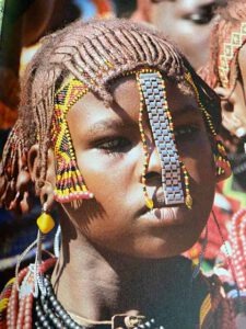 Nahaufnahme eines jungen Mädchens mit kunstvoll geflochtenen Zöpfen und buntem Perlenschmuck im Haar, traditioneller afrikanischer Stil.